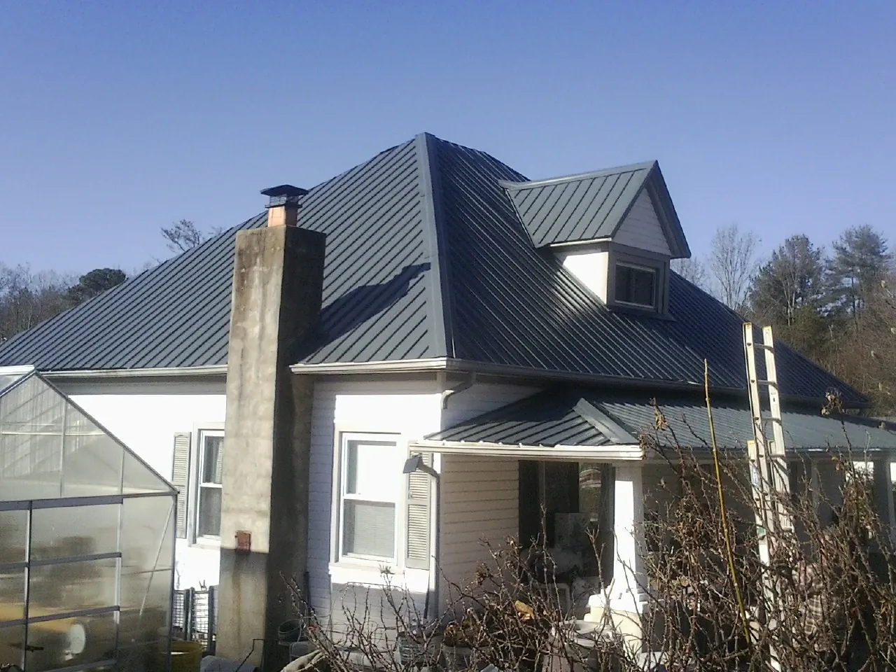 Dark blue standing seam metal roof on a white farmhouse with dormer — Slate & Tile Roof Repair by Roofing Brothers in Burlison