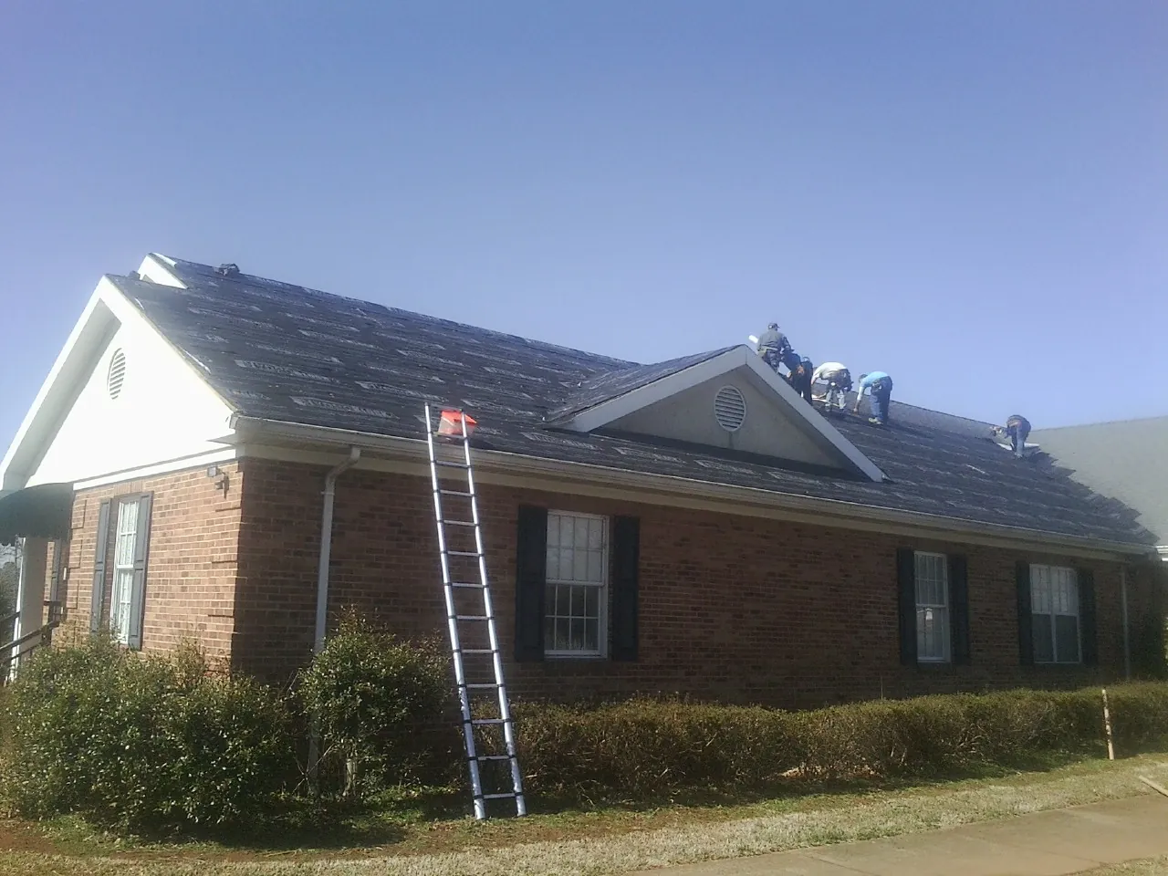 Crew tearing shingles off a brick ranch roof with a ladder set — Metal Roof Repair work by our crew in Burlison