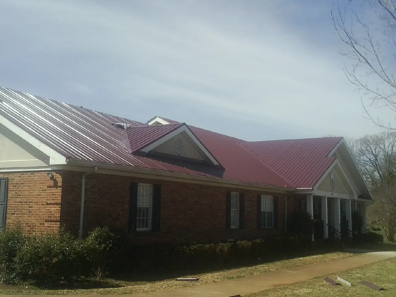 Red metal roof with gabled entries on a long brick building, from a Hail Damage Roof Repair job in Burlison