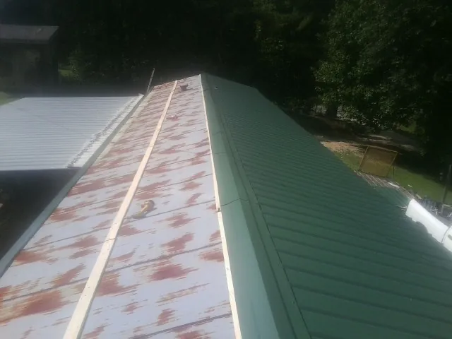 Old rusted panels beside newly installed green metal roofing — Wind Damage Roof Repair by Roofing Brothers in Burlison