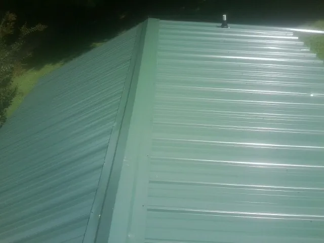 New green metal panels meeting at the ridge of a roof — Flat Roof Repair work by our crew in Burlison