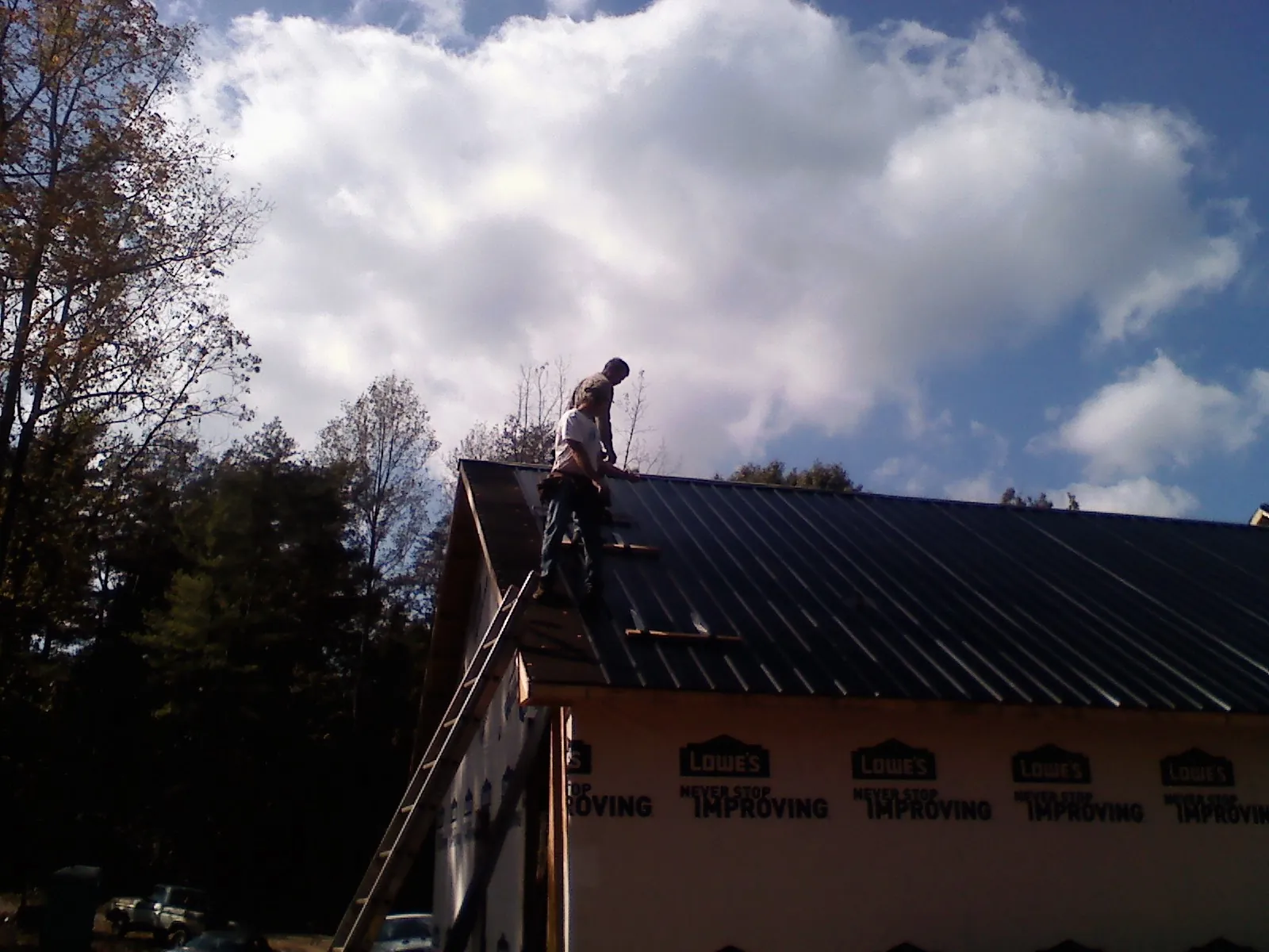 Roofer fastening dark metal panels high against a cloudy sky, from a Roof Inspection job in Burlison