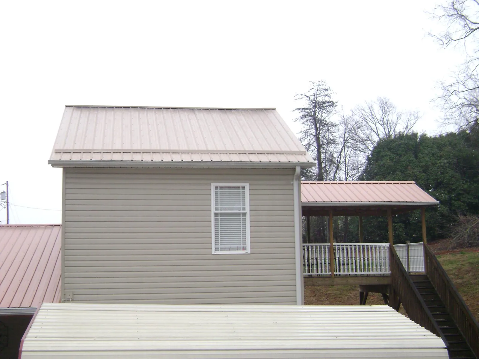 Tan metal roofs on a two story addition and attached porch, from a Roof Replacement job in Burlison